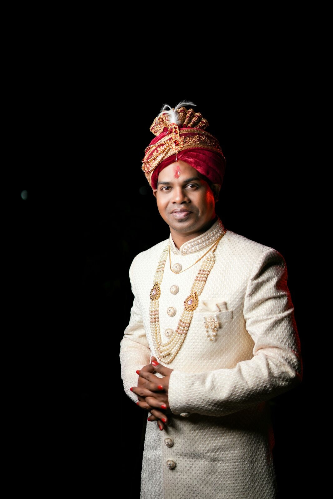 Man in traditional white sherwani with red turban against a black background
